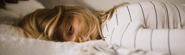 Frau liegt mit Unterleibschmerzen und Erschöpfung auf dem Bauch im Bett.